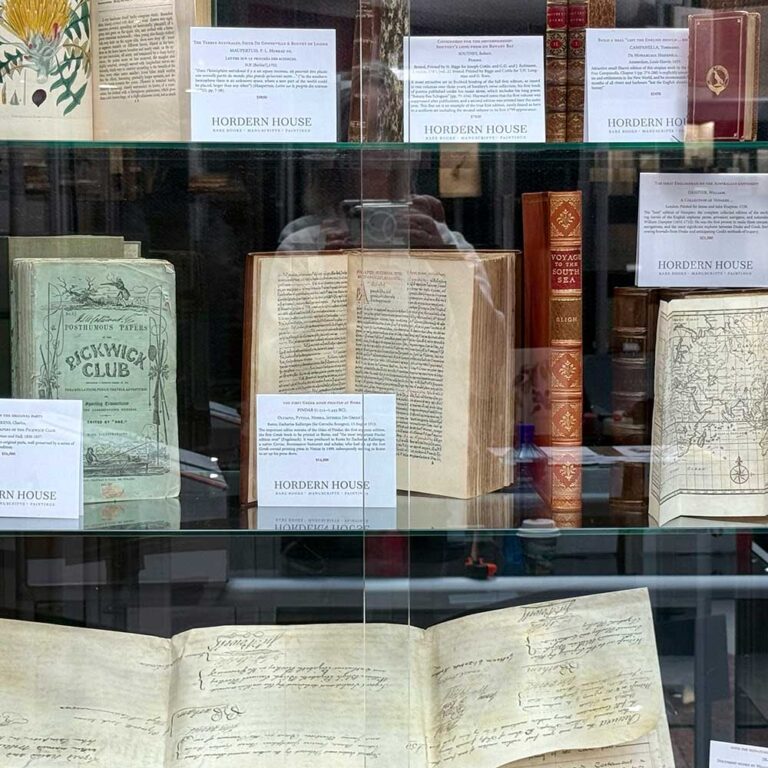 Antiquarian books, early voyage accounts and a folding map displayed in a glass case at the Sydney Rare Book Fair.