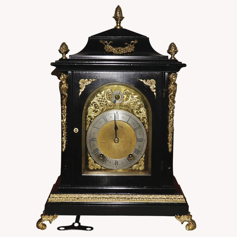 English Georgian revival table clock in ebony and ormolu, 8-day movement by Winterhalder & Hofmeier, ¼ hour Bim Bam chime on 2 metal gongs, roman numerals on silvered dial, rate adjusting dial. 42cm x 30cm x 21cm, weight 6.6kg. Complete and working.