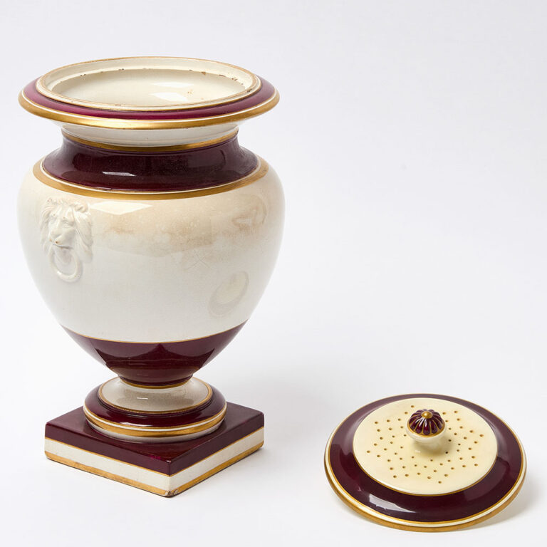 A cream and burgundy glaze pedestal form leech jar with gilt lettering and a cartouche decoration